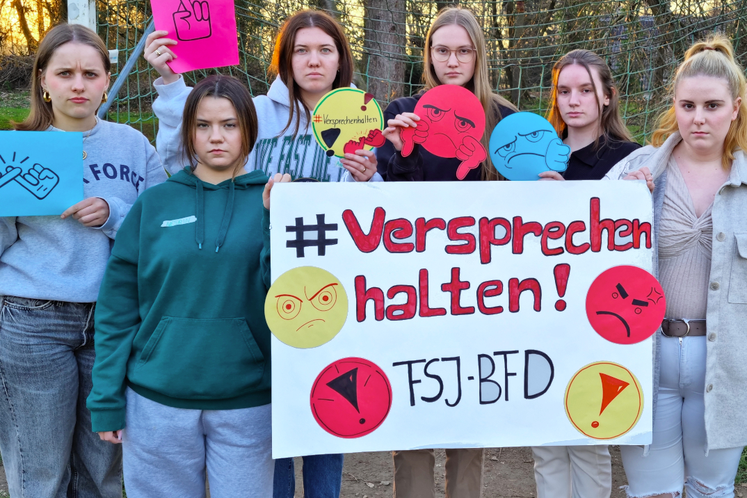 6 junge FSJlerinnen halten ein Schild mit der Aufschrift: "Versprechen halten! FSJ/BFD" in die Kamera